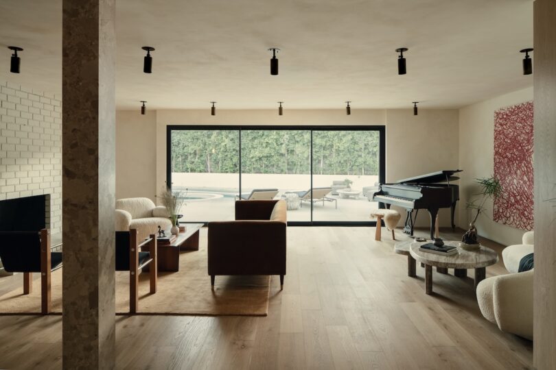 A modern living room with a grand piano, contemporary furniture, large glass doors, and a view of greenery.