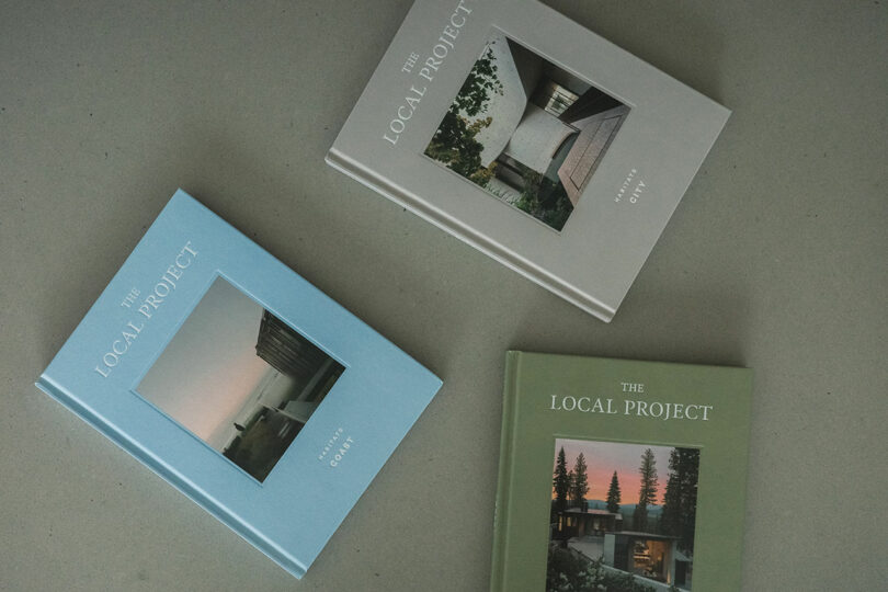 Three hardcover books titled "The Local Project," in grey, blue, and green, each featuring a modern architectural cover photo. The designs subtly echo the innovative style of Amanda Gunawan, offering a glimpse into contemporary architectural marvels.