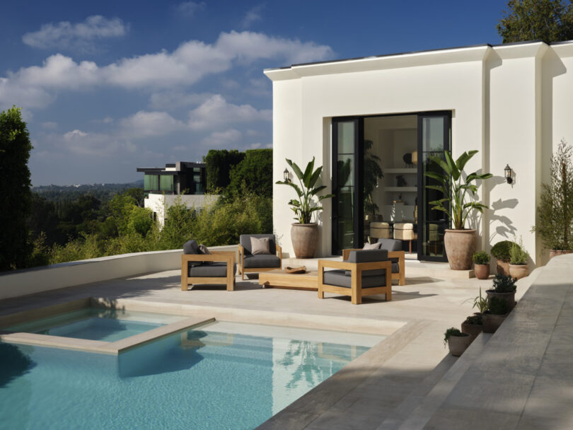 Modern outdoor patio designed by Studio OSKLO featuring a pool and seating area with wooden furniture and potted plants. A white building with large windows is in the background under a clear sky.