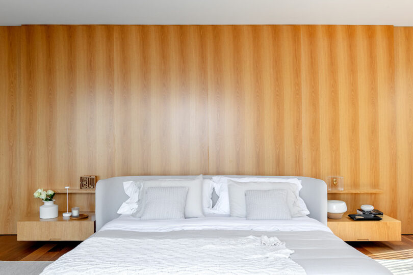 A minimalist bedroom with a wooden accent wall, a modern bed with white and grey bedding, and two floating nightstands holding small decor items.