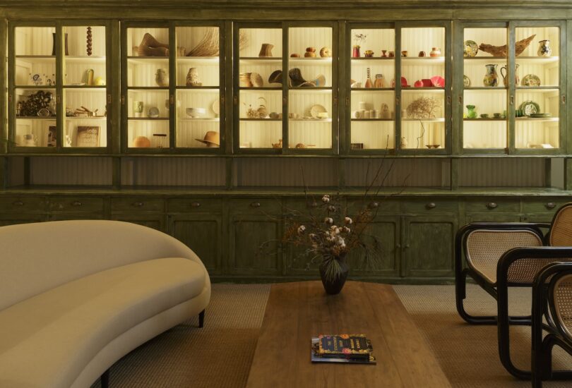 Common area featuring a 7-meter-wide grocer’s cabinet with illuminated shelves displaying eclectic items, complemented by a curved beige sofa and wooden coffee table