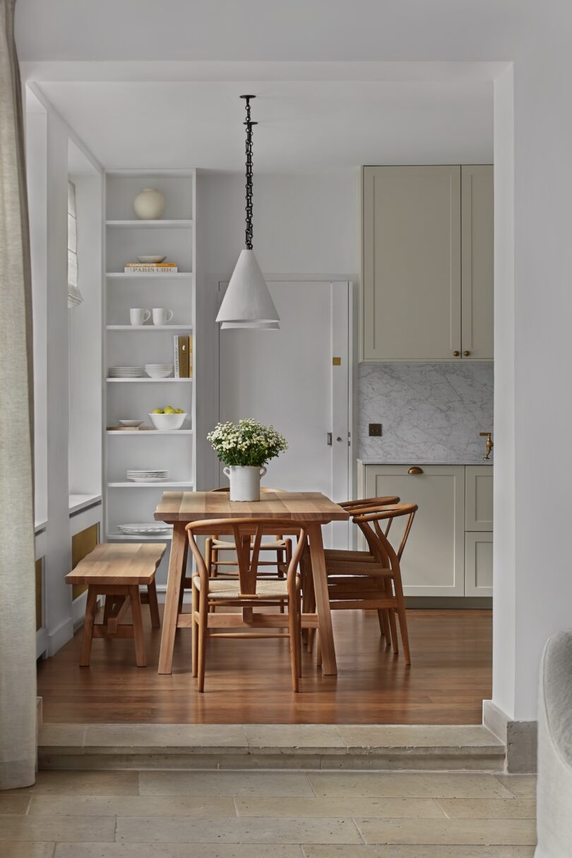 A minimalist Parisian kitchen with a warm wooden dining table, and Wishbone chairs